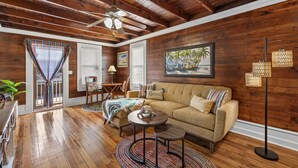 Una sala de estar acogedora con pisos de madera, un sofá color beige, un ventilador de techo y un cuadro con una escena de playa.