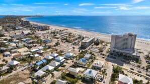 Vista aérea de un pueblo costero con un hotel frente a la playa, edificios residenciales y un océano azul cristalino.