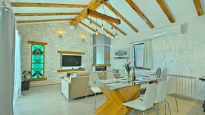 Un salon moderne avec une cheminée en pierre, un téléviseur fixé au mur et un coin repas comprenant une table et des chaises en verre.