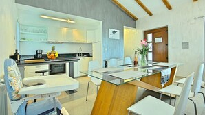 Une cuisine moderne avec des meubles blancs, une table à manger en verre et un plafond en bois.