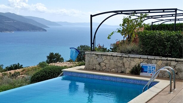 A swimming pool with a stone wall and a metal pergola, overlooking a body of water and distant mountains. - Stunning home in Brsec with sauna (Brsec)