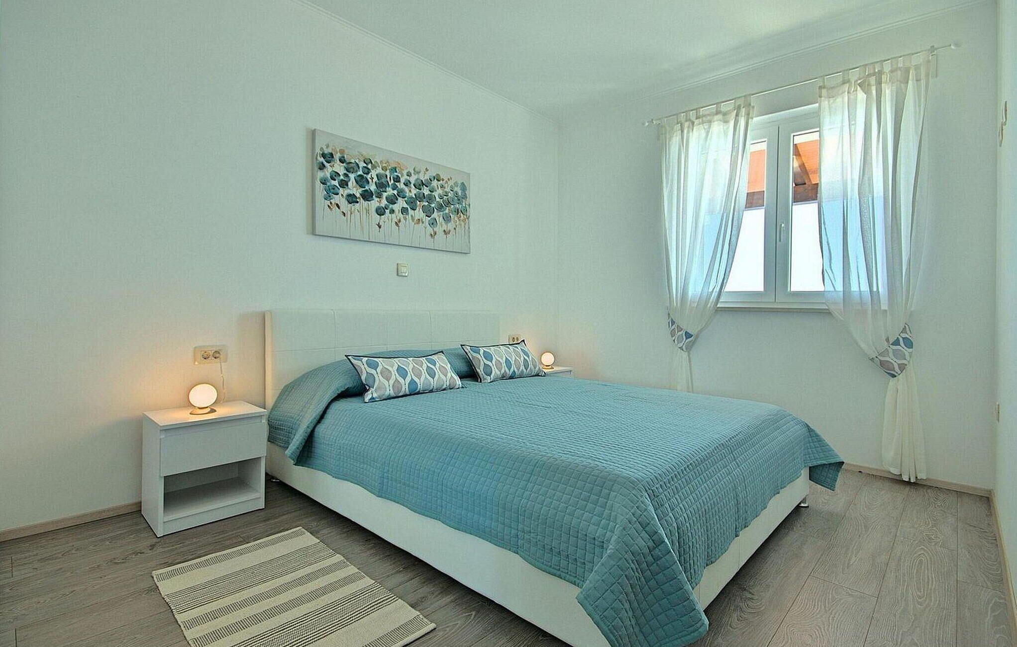 Une chambre à coucher comprenant un lit, une table de chevet, une commode, une fenêtre avec des rideaux et une œuvre d’art accrochée au mur.