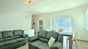 A modern living room with a grey sofa, a dining table, and a view of the outside. - Stunning home in Brsec with sauna (Brsec)