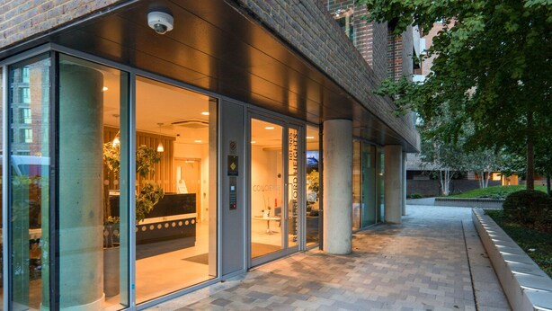 L’entrée d’un hôtel, avec un comptoir d’accueil, des portes vitrées et une façade en briques.