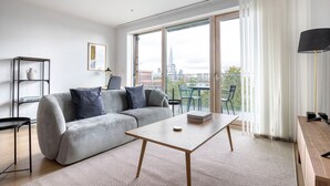 Un salon moderne avec un canapé gris, une table basse en bois et une vue sur la ville grâce à de grandes fenêtres.