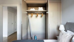 Une chambre à coucher avec un lit, une armoire où sont suspendus des vêtements et une planche à repasser.