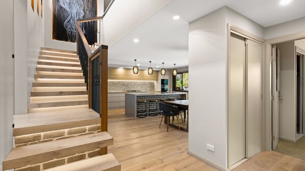 A modern kitchen with a central island, wooden staircase, and pendant lighting.