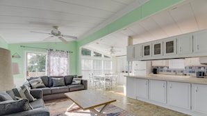 A spacious living area with a sofa, coffee table, and dining table. A kitchen with white cabinets and a refrigerator is visible in the background. - Venture Out 2 Bedroom (Cudjoe Key)