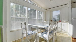 A bright kitchen with white cabinetry, a dining table with chairs, and large windows with blinds. - Venture Out 2 Bedroom (Cudjoe Key)