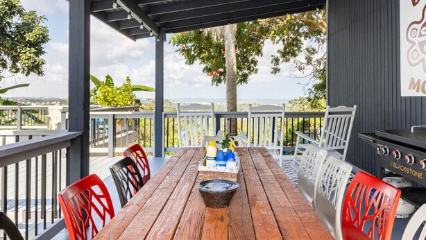 An outdoor patio with a wooden table, red and white chairs, a grill, and a view of the landscape. - Bello Monte Retreat House with Pool in El Yunque (Hato Candal)
