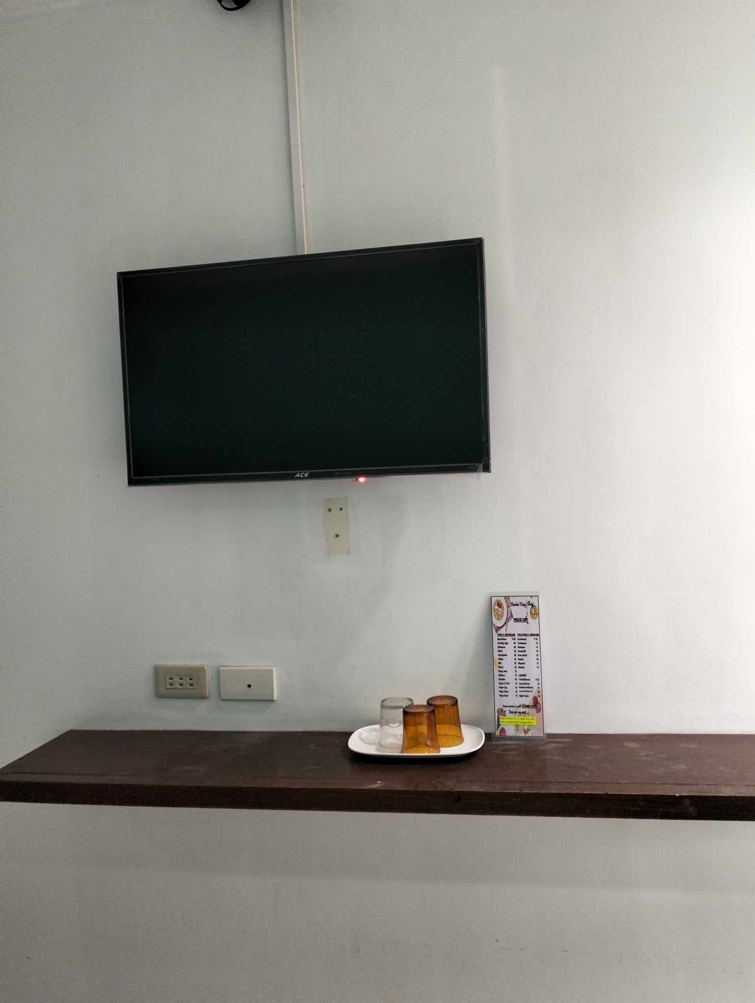 A television mounted on a wall, a power outlet, and a small table with a plate and a menu.