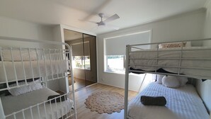 Una habitación con dos literas, ventilador de techo, un ventanal grande y un tapete tejido.