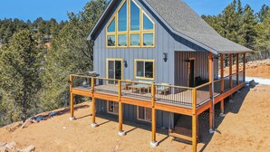 Une maison à deux étages, dotée d’un balcon et d’une terrasse, entourée d’arbres et surplombant un ciel dégagé.