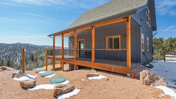 Une cabane dotée d’une terrasse en bois, de grandes fenêtres et offrant une vue sur les montagnes.