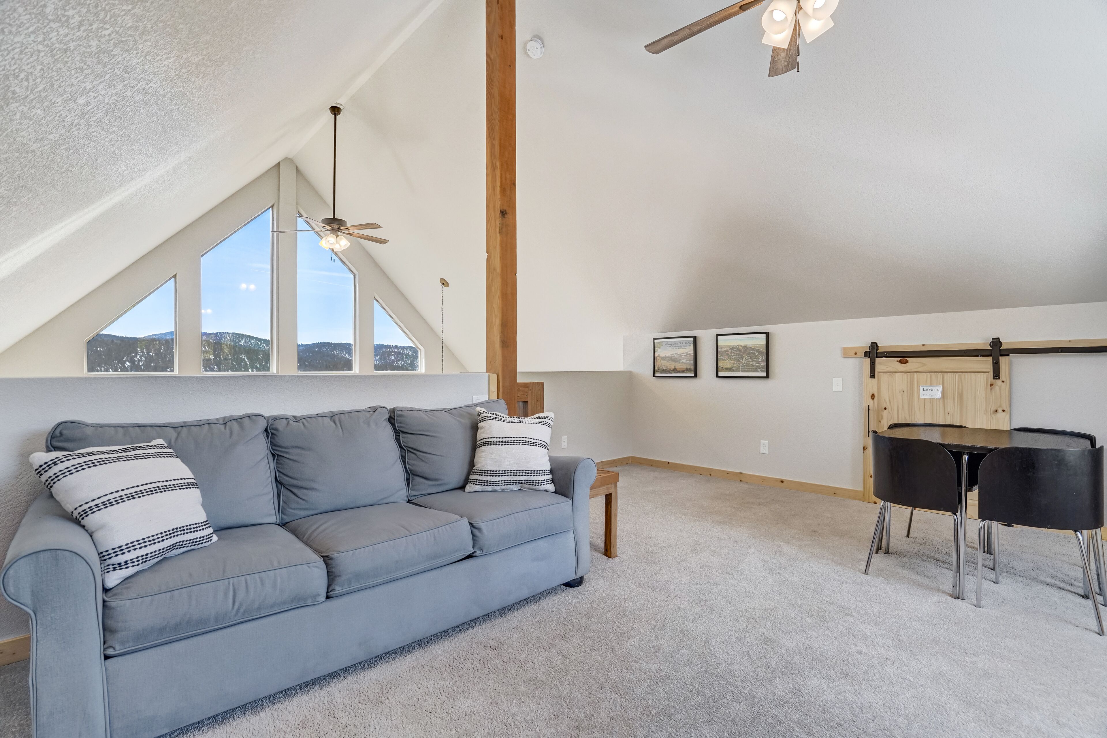 Une pièce de style loft avec un canapé gris, une table à manger avec des chaises et une grande fenêtre donnant sur les montagnes.