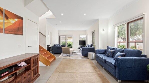 A spacious living room with a sofa set, a TV, and a staircase leading to another room.