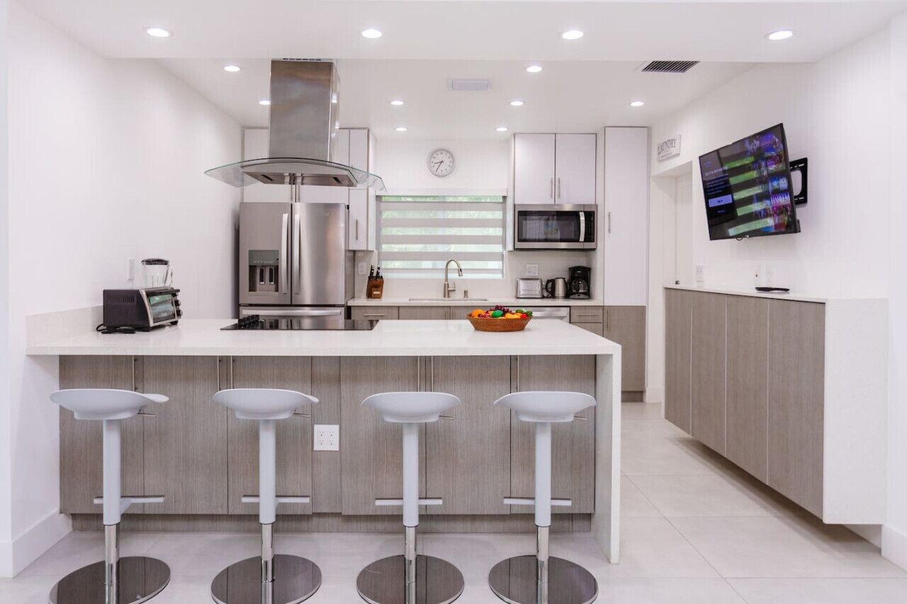 A modern kitchen with a central island, bar stools, a microwave, and a flat-screen TV.