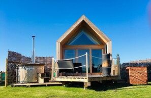 Eine Holzhütte mit einem Giebeldach, großen Fenstern und einer Terrasse mit Sitzgelegenheiten.