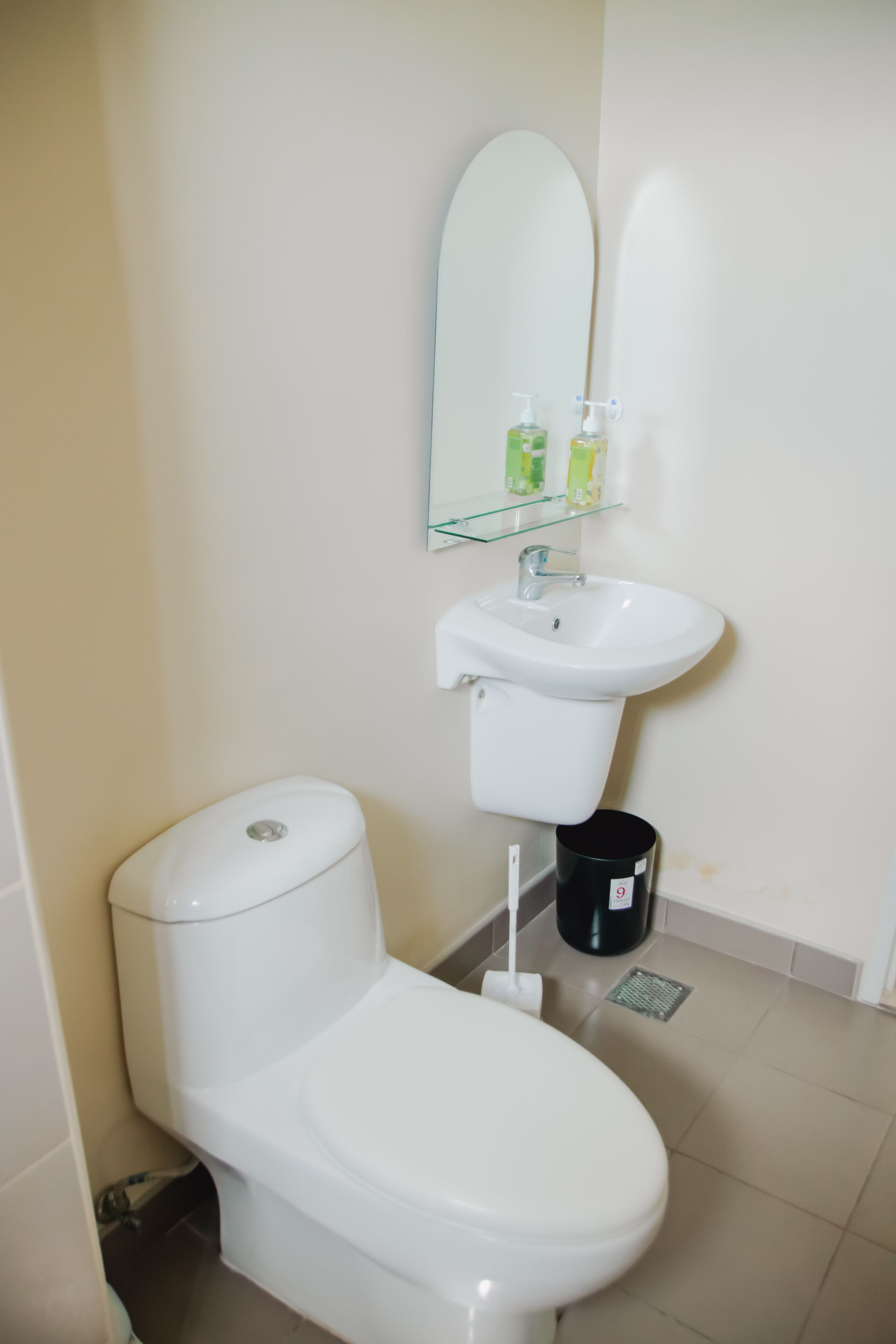 A bathroom with a toilet, a sink, a mirror, and a trash bin.