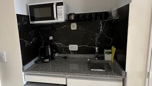 Et kompakt tekøkken med indbygget mikrobølgeovn, kaffemaskine og et lille køleskab.