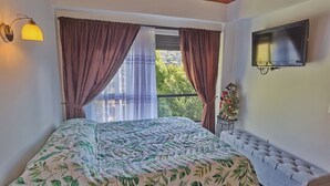 Une chambre à coucher avec un lit, une télévision, une fenêtre avec des rideaux et une petite table ornée de fleurs.