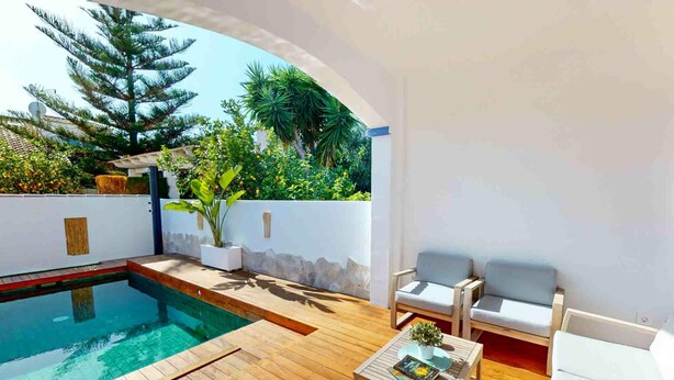 Un espace piscine avec une terrasse en bois, un coin salon avec des chaises blanches et une vue sur la verdure et les arbres.