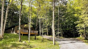 Eine Holzhütte mit einer Holzdiele und einem Schotterweg, umgeben von hohen Bäumen.