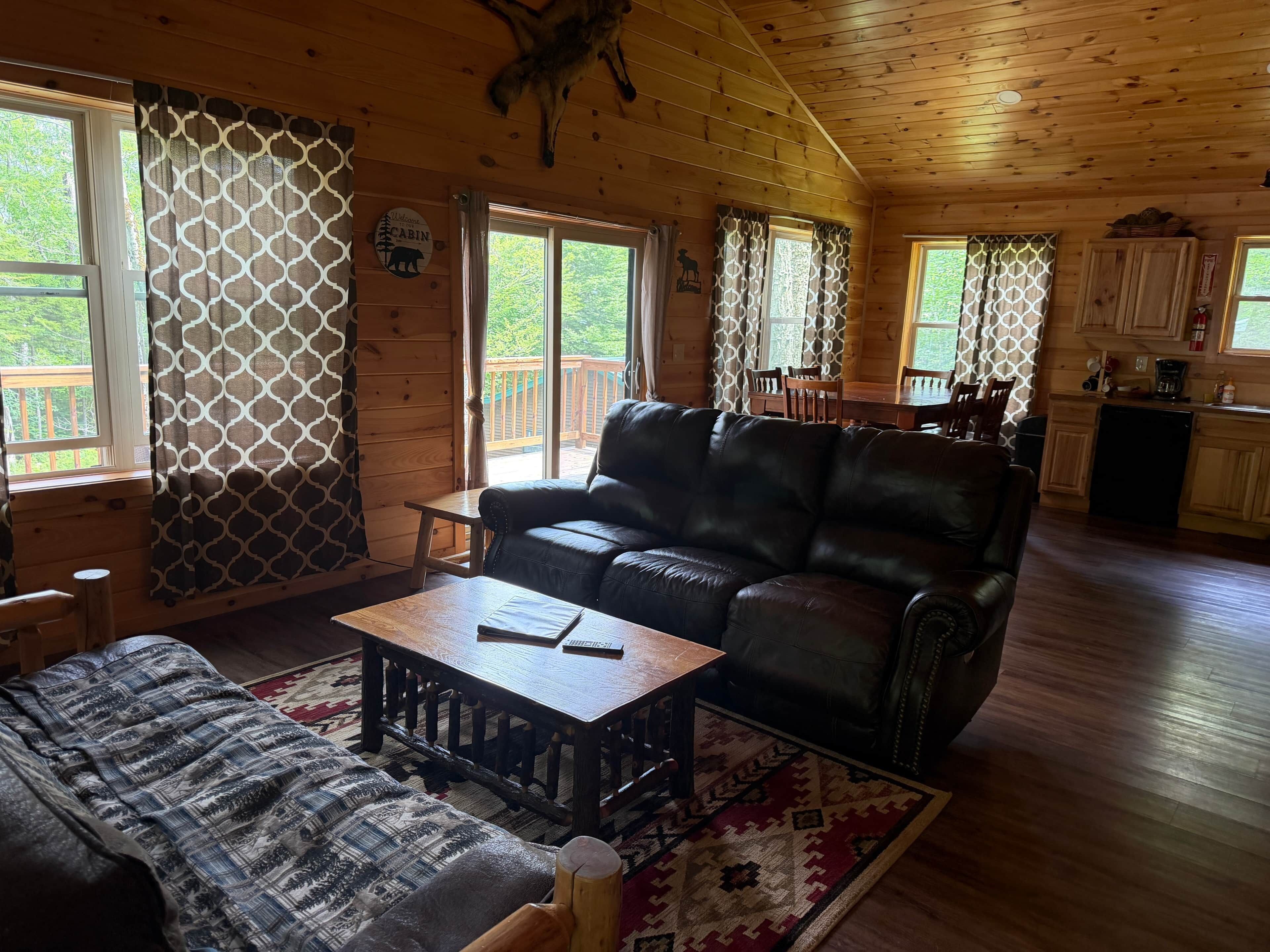 A cabin interior with a leather sofa, wooden dining table, and a kitchen area.