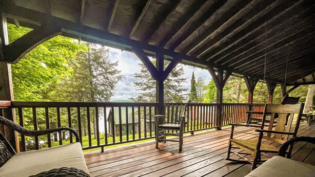 Une terrasse en bois avec des sièges extérieurs, donnant sur un lac et entourée d’arbres.