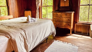 Une pièce en bois avec un lit, une commode et une fenêtre donnant sur des arbres.