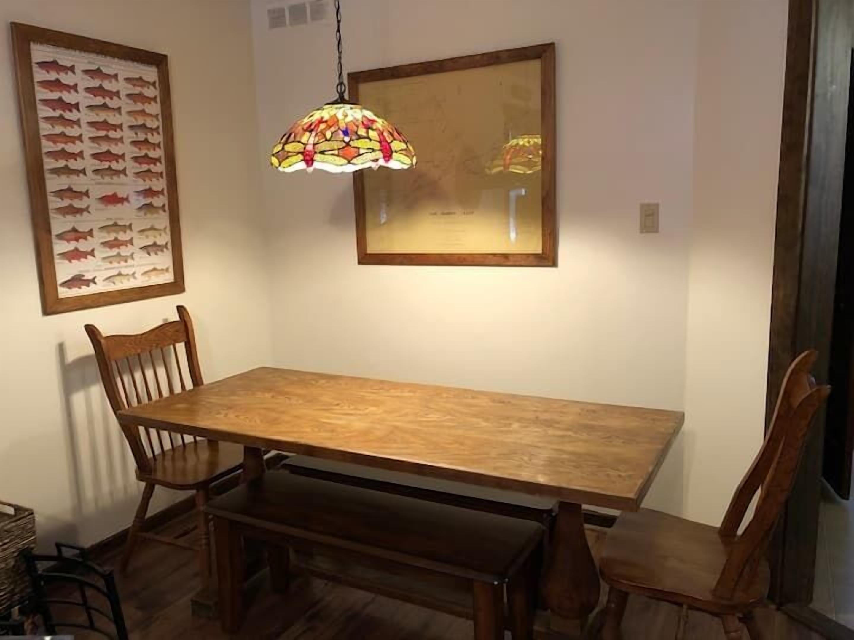 Comedor con mesa de madera, cuatro sillas, un banco, una lámpara colgante de vitral e ilustración enmarcada de un pez en la pared.