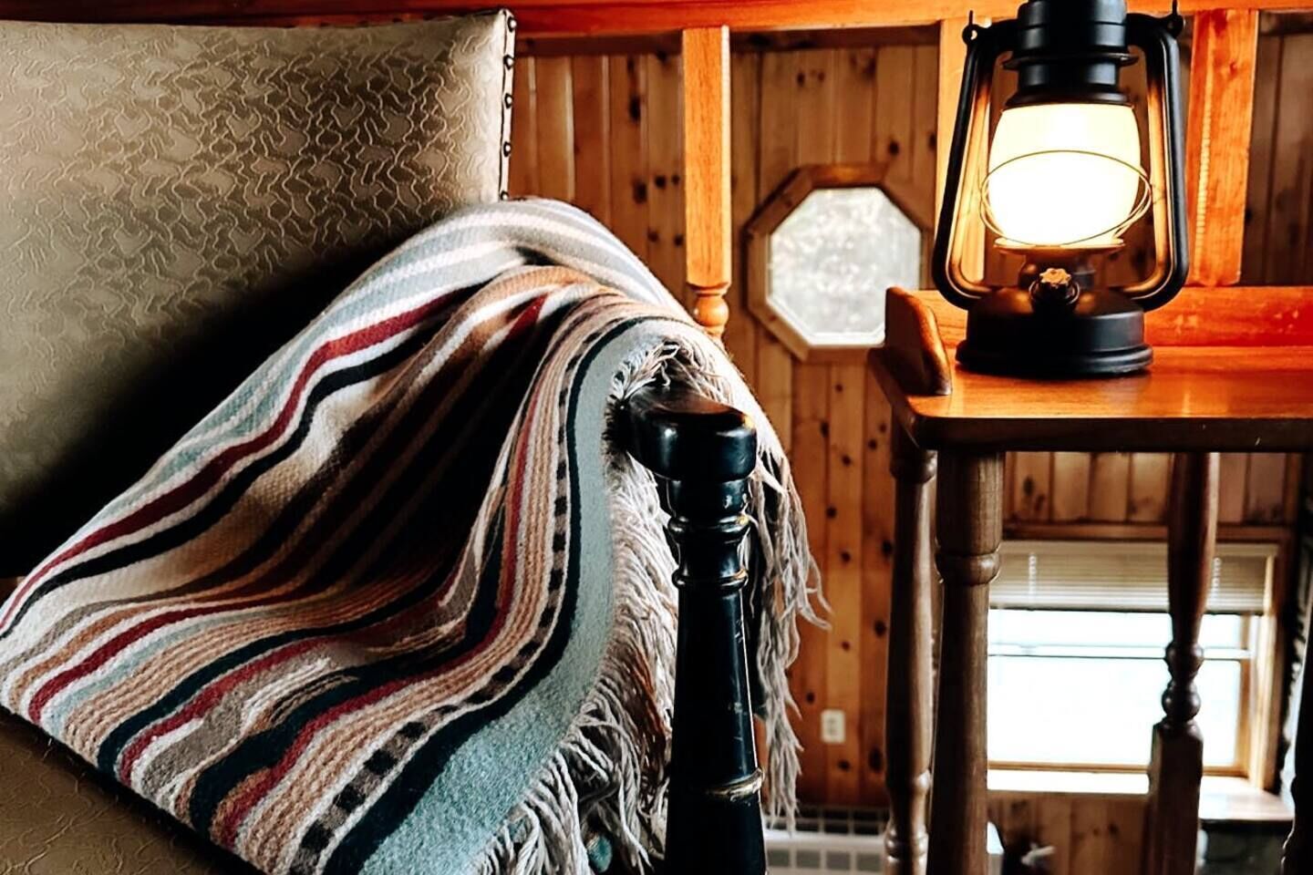A cozy room with a wooden interior, a patterned blanket draped over a chair, and a table with a lantern.