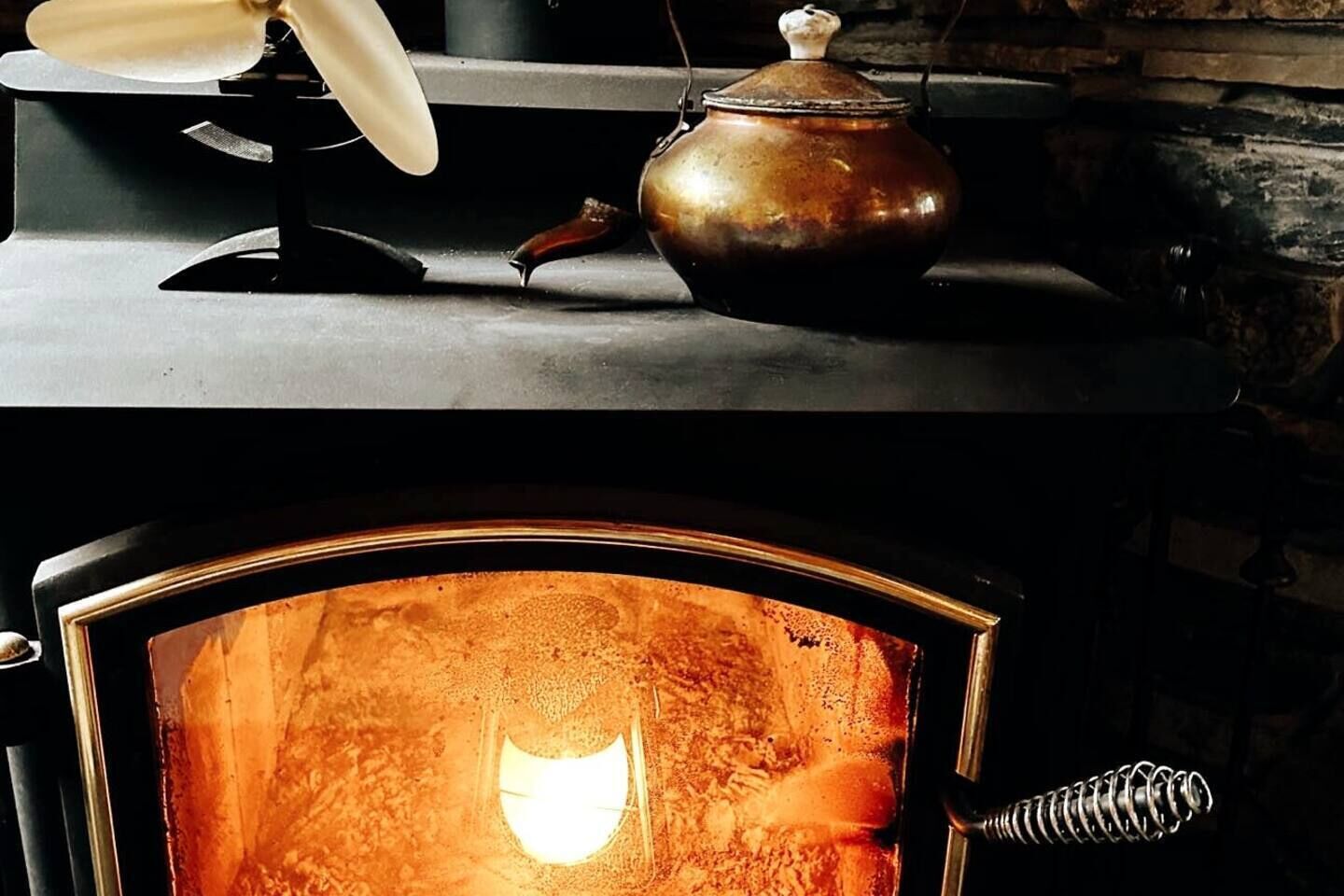 Una estufa de leña tradicional con fuego a la vista, una tetera encima y una chimenea.