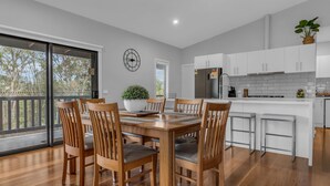 A modern kitchen with white cabinets, a stainless steel refrigerator, and a dining area with wooden chairs and a large table.
