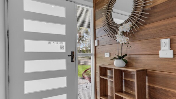A modern entrance with a grey door featuring multiple panels, a wooden wall with a decorative mirror, and a potted orchid.