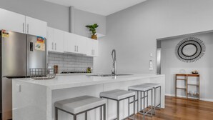 A modern kitchen with a central island, bar stools, a stainless steel refrigerator, and a backsplash.