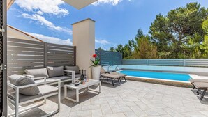 En udendørs terrasse med pool, siddeområde og en høj bygning.