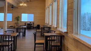 A spacious wooden interior with multiple tables and chairs, large windows offering views of a snowy landscape, and a chandelier hanging from the ceiling. - View! View! View! Relax in Nature!  (Fairbanks)