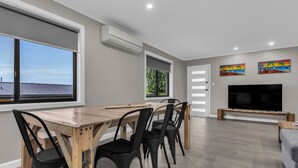 Una sala de estar moderna con una mesa de comedor de madera, sillas negras, un televisor de pantalla plana y obras de arte en las paredes.