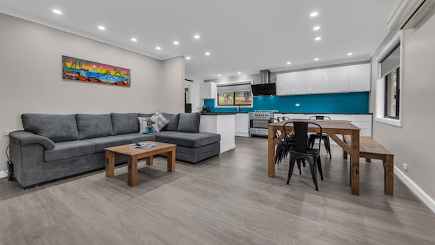 Una sala moderna con un sofá gris, una mesa de centro de madera y un comedor con una mesa y sillas de madera.