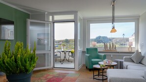 A modern living room with a sofa, a green armchair, a small table, and a potted plant. - Wohnung Stella - Am Strand- Wohnung Stella (Westerland)