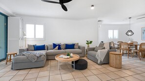 A modern living room with a grey sofa, blue cushions, a round coffee table, and a dining area with wooden chairs and a table. - Central Location Stylish 3 Bed Pool - Sunshine Central (Sunshine Beach)