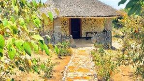 A thatched-roof hut with a stone pathway leading to it, surrounded by greenery. - Eco Mara Tented Camp  (Maasai Mara)