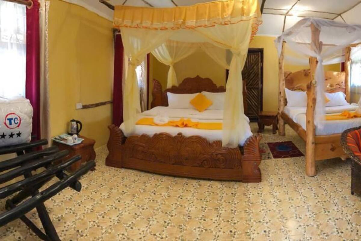 A room with two wooden beds with canopy beds, a wooden bench, a small table, and two wicker chairs.