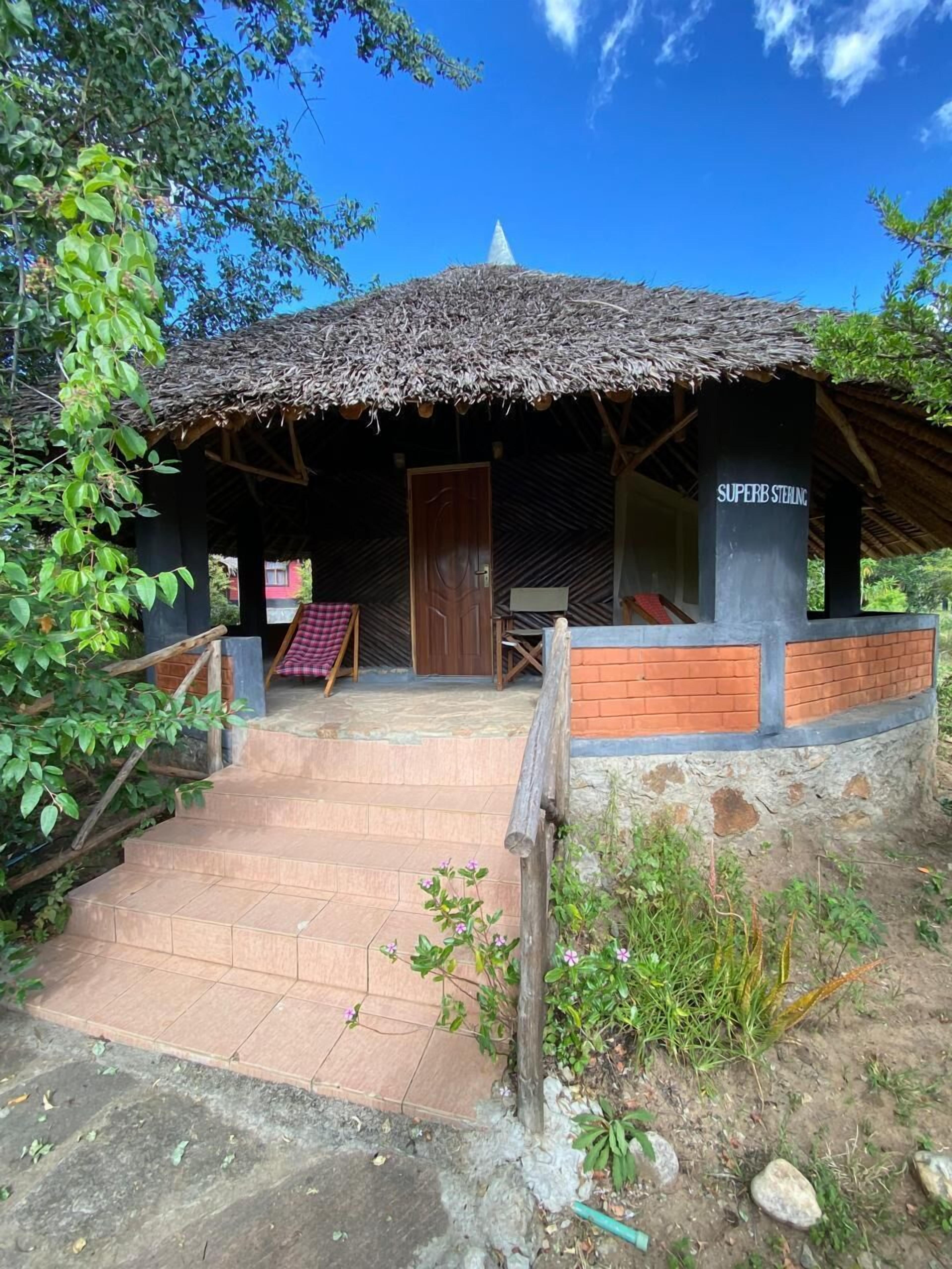 A rustic building with a thatched roof, a wooden door, and a sign reading "SUPERB STEAMING."