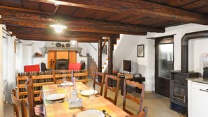 Een eethoek met een houten tafel gedekt voor vier personen, omringd door houten stoelen. Achtergrond toont een open haard, en aan de rechterkant een modern keuken hoekje.