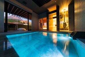 A modern indoor swimming pool with a view of a mountain landscape, a glass-enclosed area with a chair, and a shower area with a glass enclosure. - Gekkoju Yufuin (Yufu)