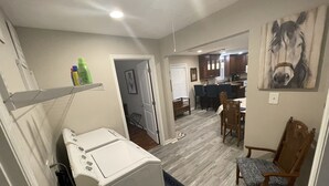 Un área de lavandería con lavadora y secadora, un comedor con mesa y sillas, y una cocina al fondo.