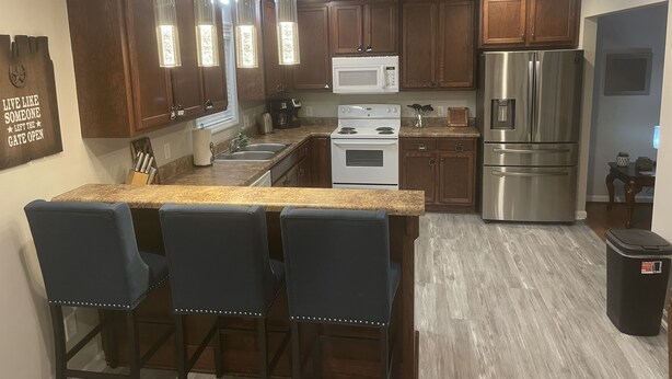 Una cocina moderna con armarios de madera, electrodomésticos de acero inoxidable, encimera de granito y una zona de bar con taburetes.