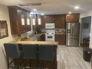 A modern kitchen with wooden cabinets, stainless steel appliances, a granite countertop, and a bar area with stools. - Comfy Country Home w/ 3 KING Beds!  (Hazel Green)